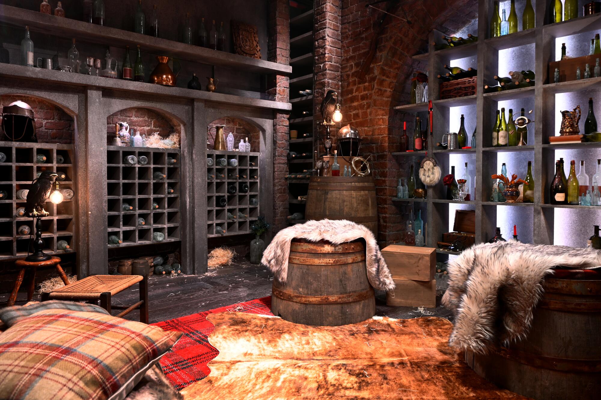 A room with racks of wine bottles and lighted shelves displaying wine bottles, plus wine barrel decor and seats