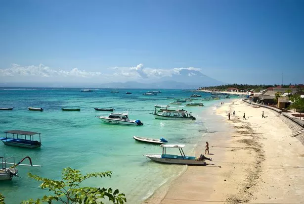 Boats moored along a tropical island beach beside a fishing village.
