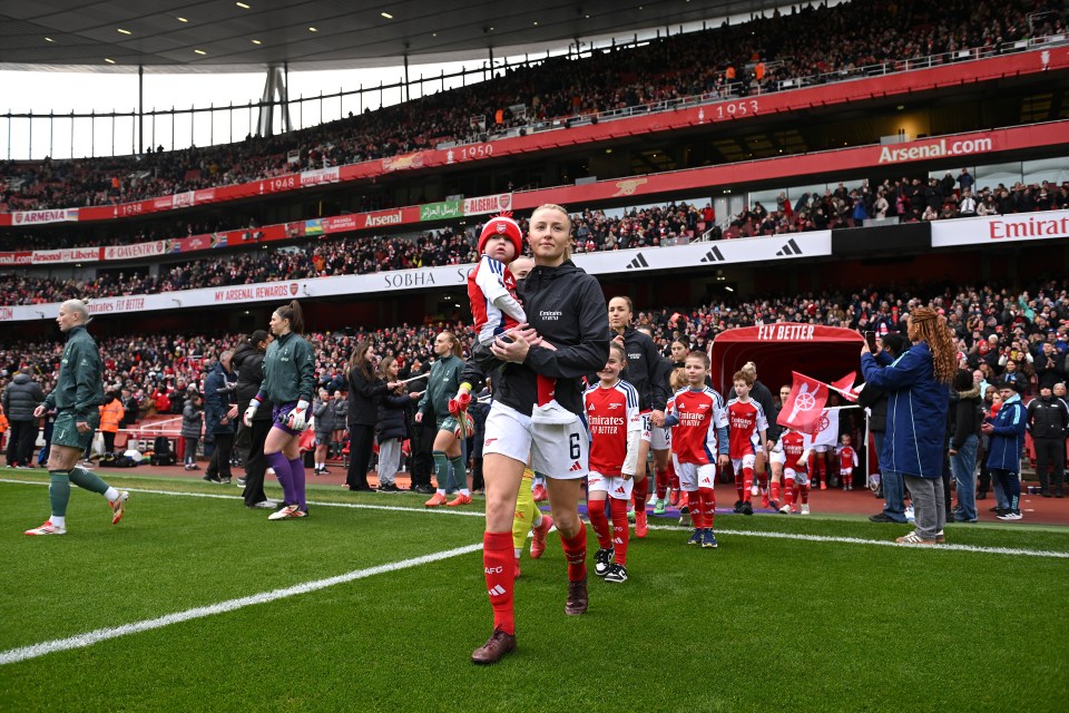 Leah Williamson of Arsenal carries a mascot onto the pitch.