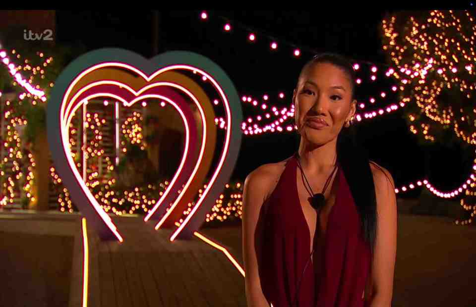 Woman in red dress standing in front of a heart-shaped light display.
