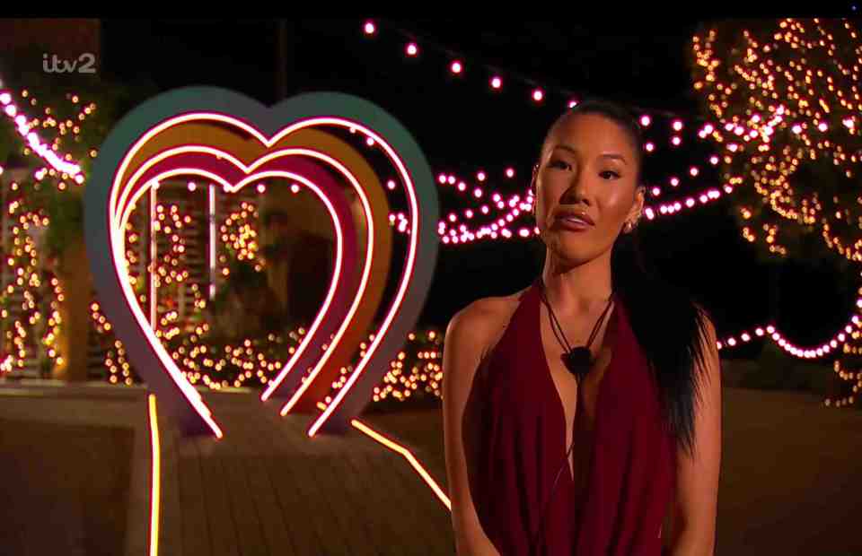 A woman stands before a heart-shaped light installation on Love Island.