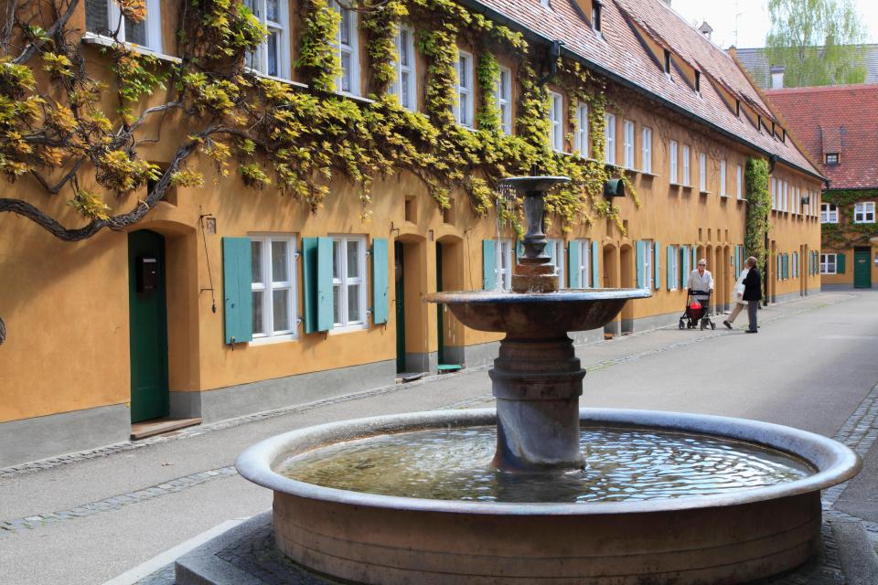 Street scene in Augsburg, Germany, showing a fountain and a row of yellow buildings with green shutters.