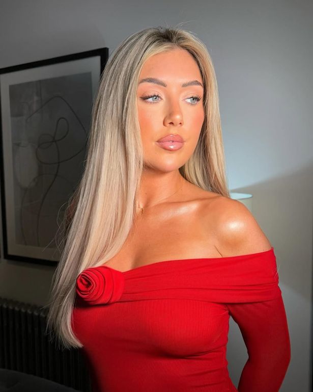 Patsy Field in a red dress stood in front of a painting on a wall.