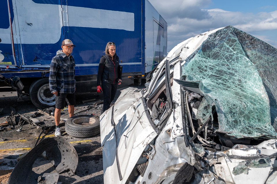 A severely damaged car after a crash, with two people inspecting the wreckage.