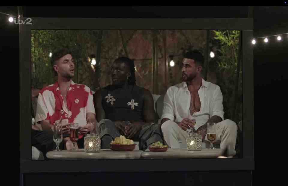 Three men watching a screen outdoors at night.