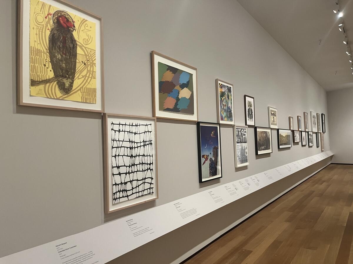 A view of a gallery shows paintings and prints laid out in a checkerboard pattern against a grey wall.