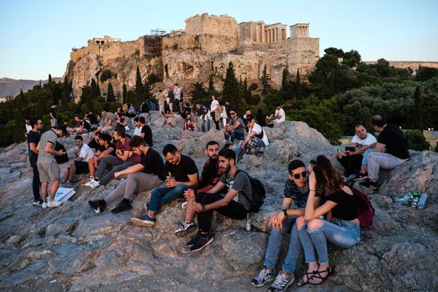 Tourists and local Athenians watch the sunset on Areopagus Hill, with the Acropolis in the background