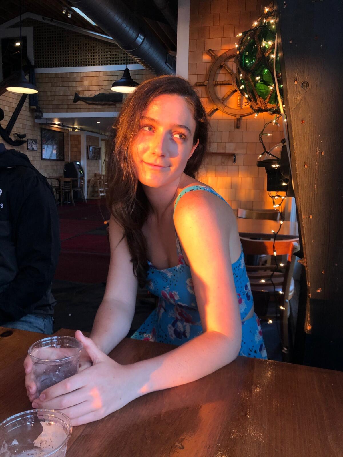 Nora Princiotti looks off to the side and holds a cup of water at a restaurant.