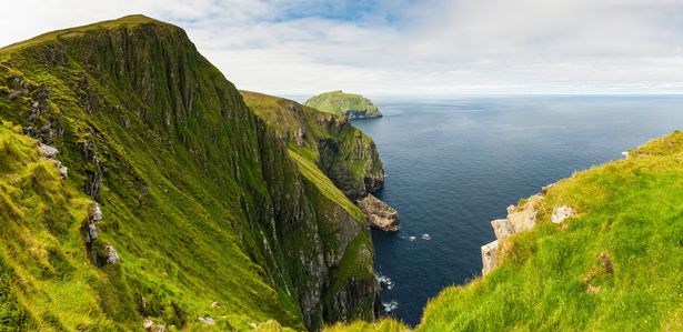 The steep cliffs and seabird colonies of Hirta being grazed by the unique Soay sheep high on the lush summer grasses above the Atlantic Ocean looking towards the island of Soay in the remote St. Kilda archipelago, the double UNESCO World Heritage Site off the Western Isles, Scotland. ProPhoto RGB profile for maximum color fidelity and gamut.