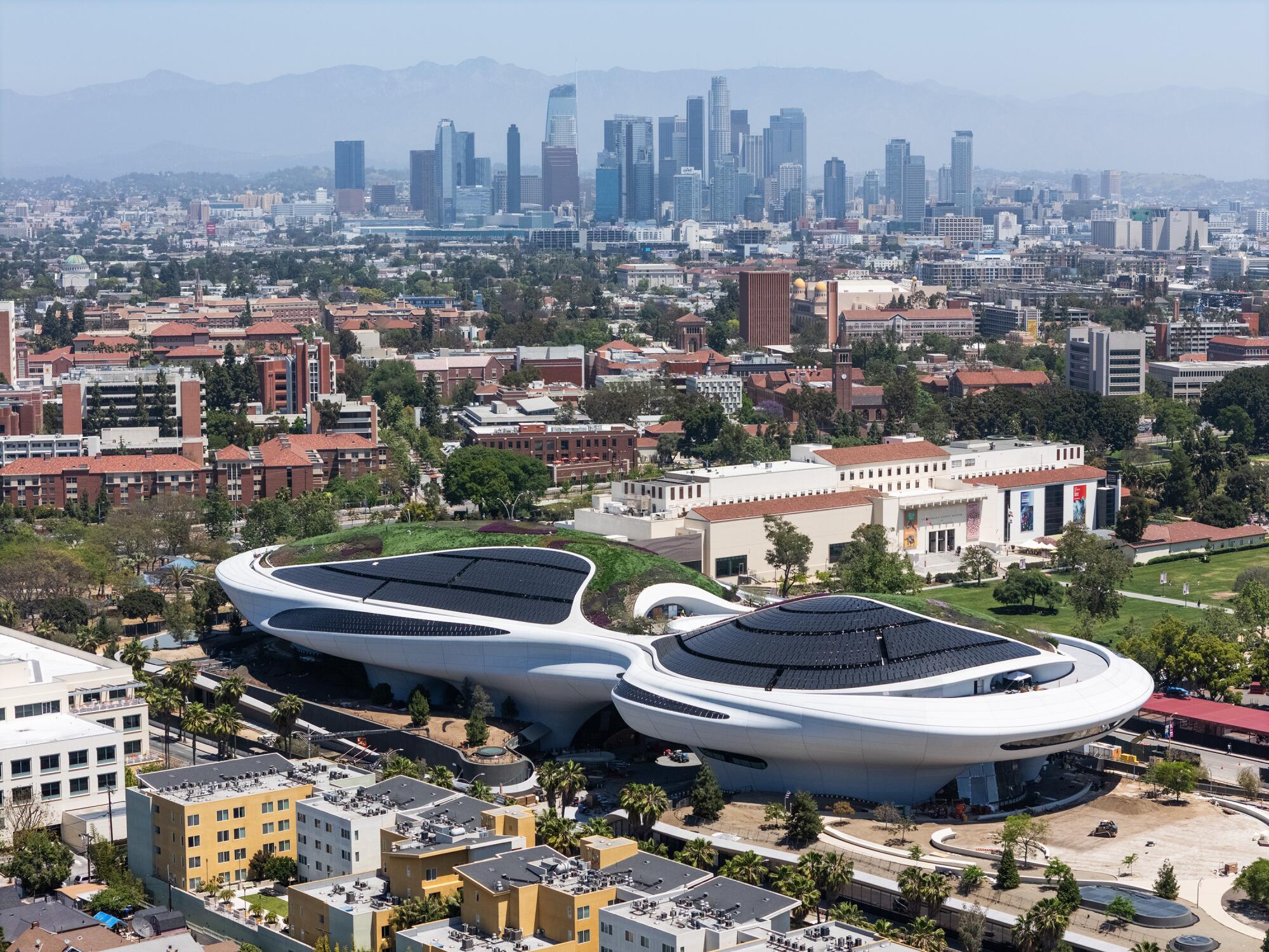 The Lucas Museum of Narrative Art rises in Exposition Park, the skyline of downtown Los Angeles rising behind it.