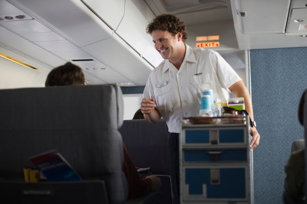 A flight attendant serves food and drink from a trolley down a plane aisle 
