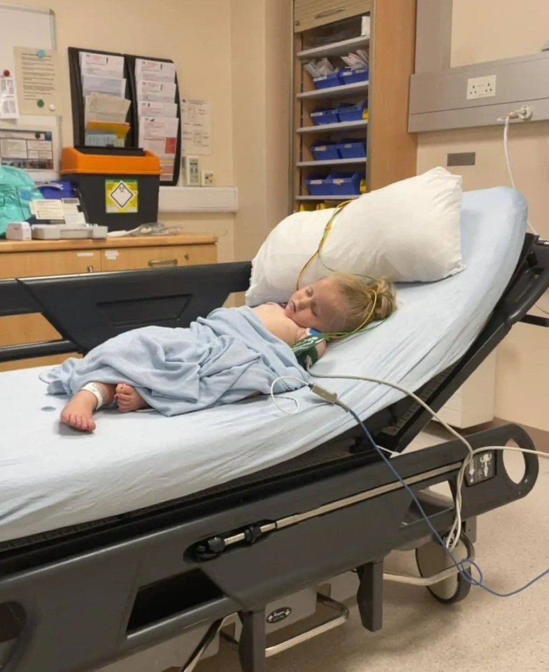 Child sleeping in a hospital bed with medical wires attached.