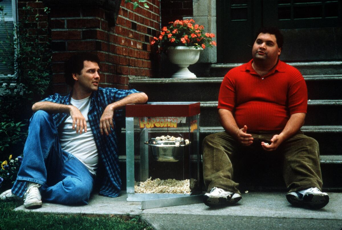 Two men sit on the outdoor stoop of an apartment.
