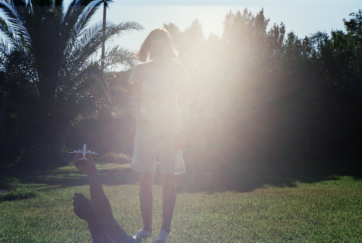 A young woman stands in silhouette in front of the sun.