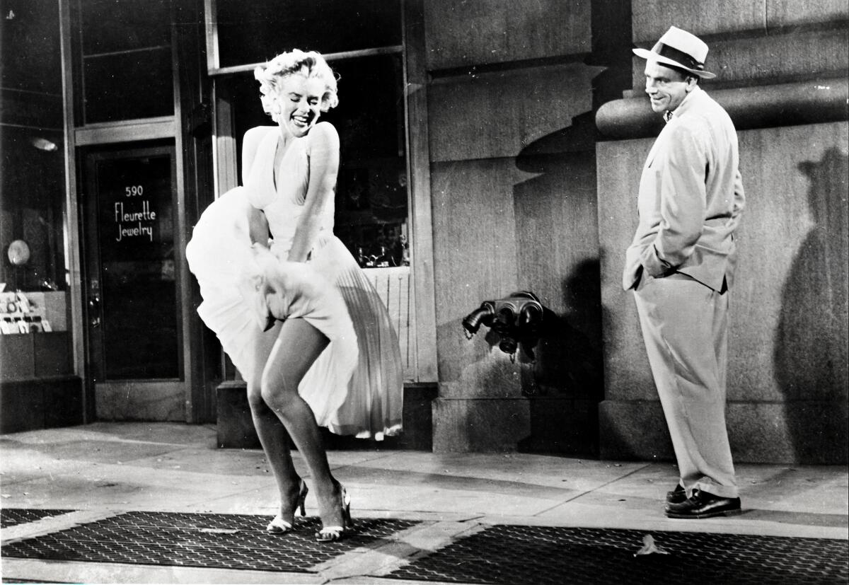 A woman smiles as her dress lifts up over a street grate while a man watches.