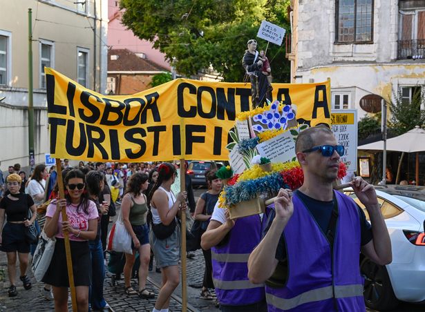 LISBON, PORTUGAL - JUNE 15: Demonstrators from "Assembleia da GraÃ§a â€“ Parar o Hotel no Quartel " and "Movimento Referendo pela HabitaÃ§Ã£o" hold an anti tourist banner as they parade behind a figure of Saint Anthony in a procession-like protest from Santo Antonio Church to Quartel de GraÃ§a joining an international protest movement against over-tourism on June 15, 2025 in Lisbon, Portugal. 
