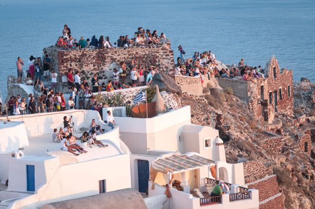 View of the Castle on the caldera of Oia in Santorini. Crowds of people perched on the half-ruined Castle and on the roofs of houses, waiting for the famous sunset.