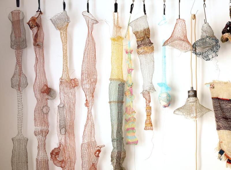 Handknitted metal sculptures hang on a wall 