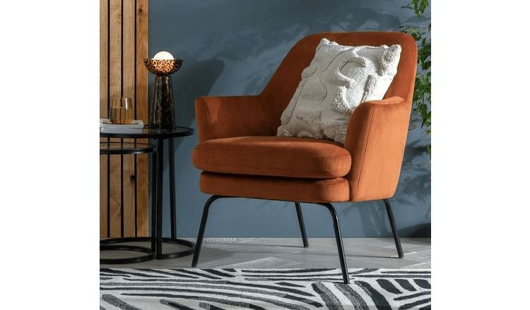 Orange velvet armchair with black legs and a cream throw pillow.