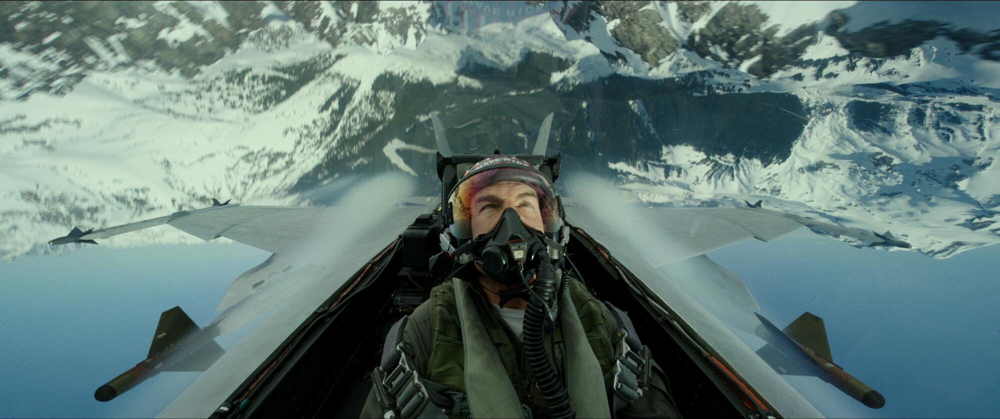 A man flies a jet over snowy terrain upside down.