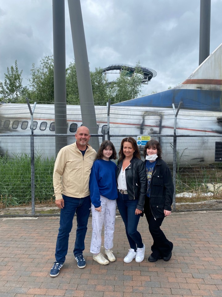 Family posing in front of a wrecked airplane at an amusement park.