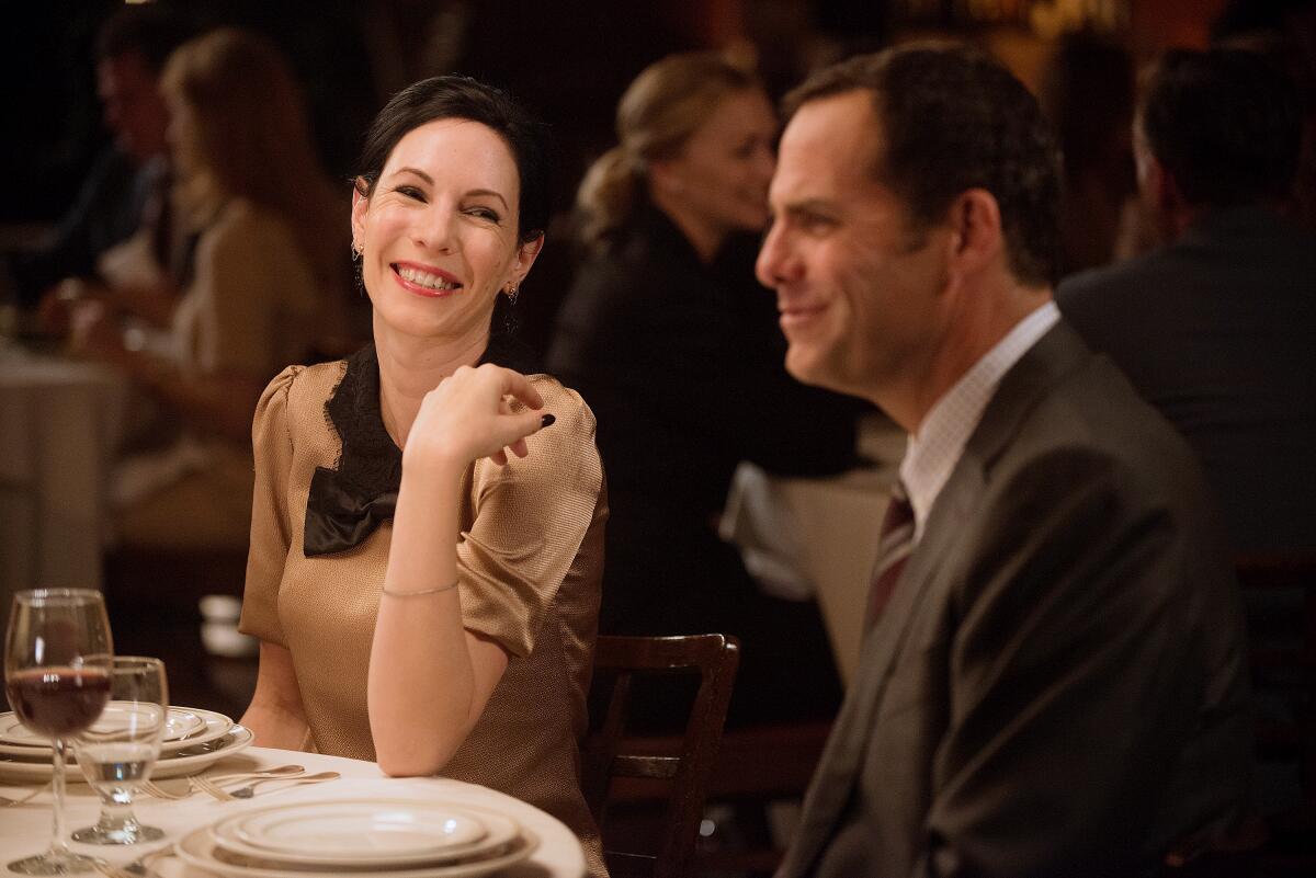 A smiling woman sits beside a man at a dinner table.