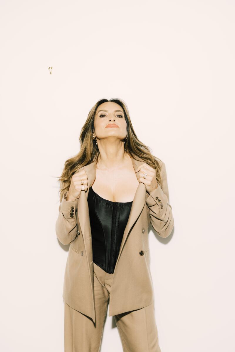 A woman in a pantsuit poses with her hands gripping her lapels