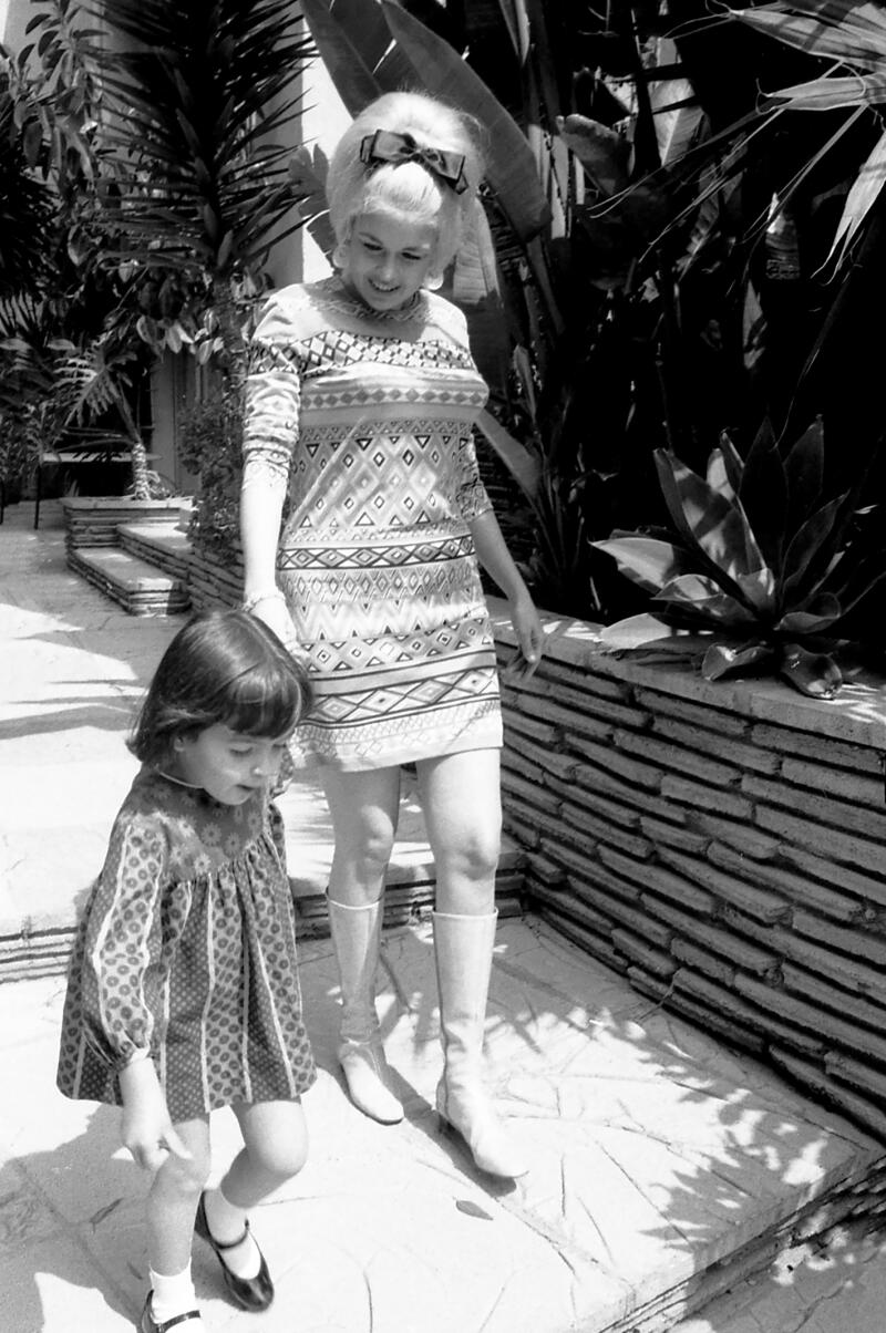 A young girl walks while holding a woman's hand.