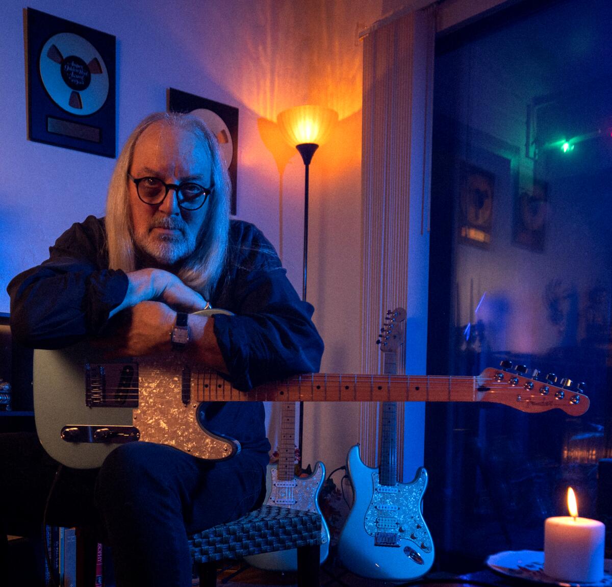 Alan Niven sits and hugs his guitar in a dimly lit room.