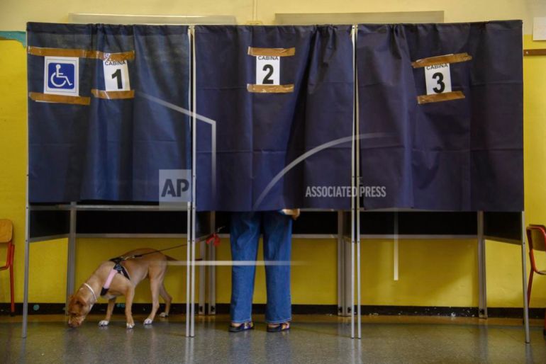 A dog on a leash waits as its owner votes in a booth for referendums on citizenship and job protections, at a polling station in Milan, Italy, Sunday, June 8, 2025. [Claudio Furlan/LaPresse via AP]