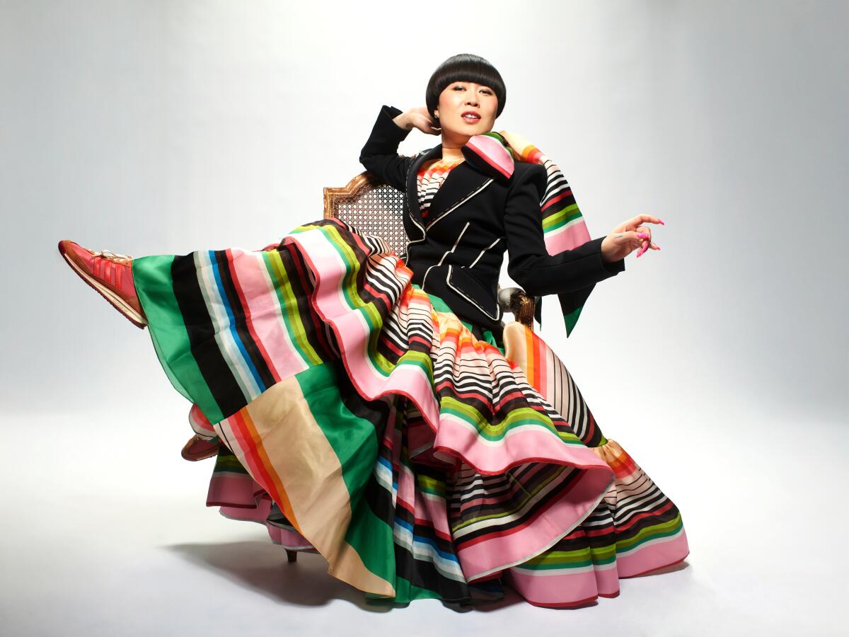 Woman with a bowlcut and multi-colored dress sits on a chair