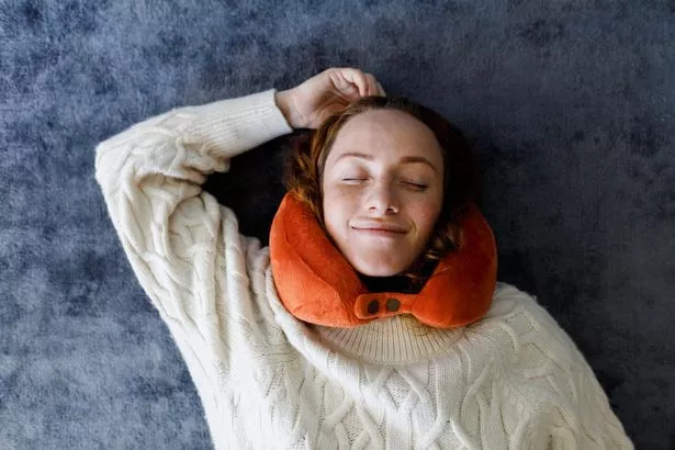 Smiling woman resting on carpet with neck pillow on