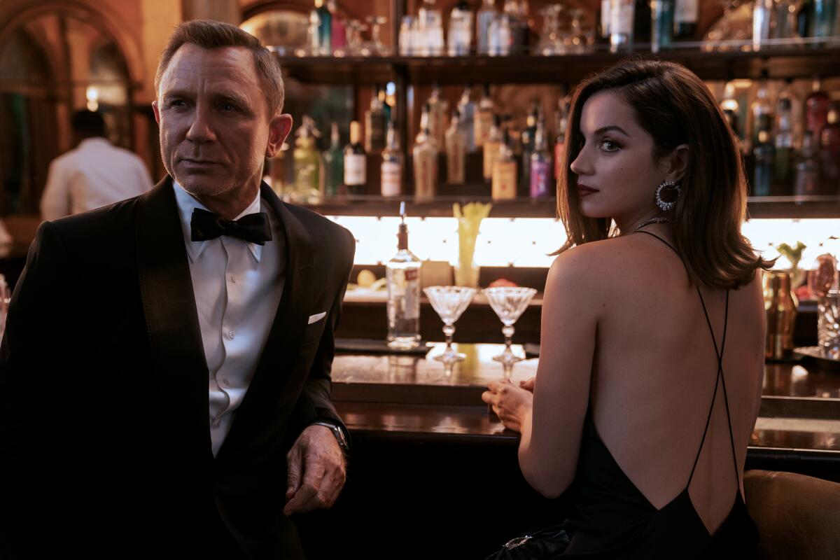 Daniel Craig, in a tuxedo, and Ana de Armas, in a black dress, stand at a bar in "No Time to Die."