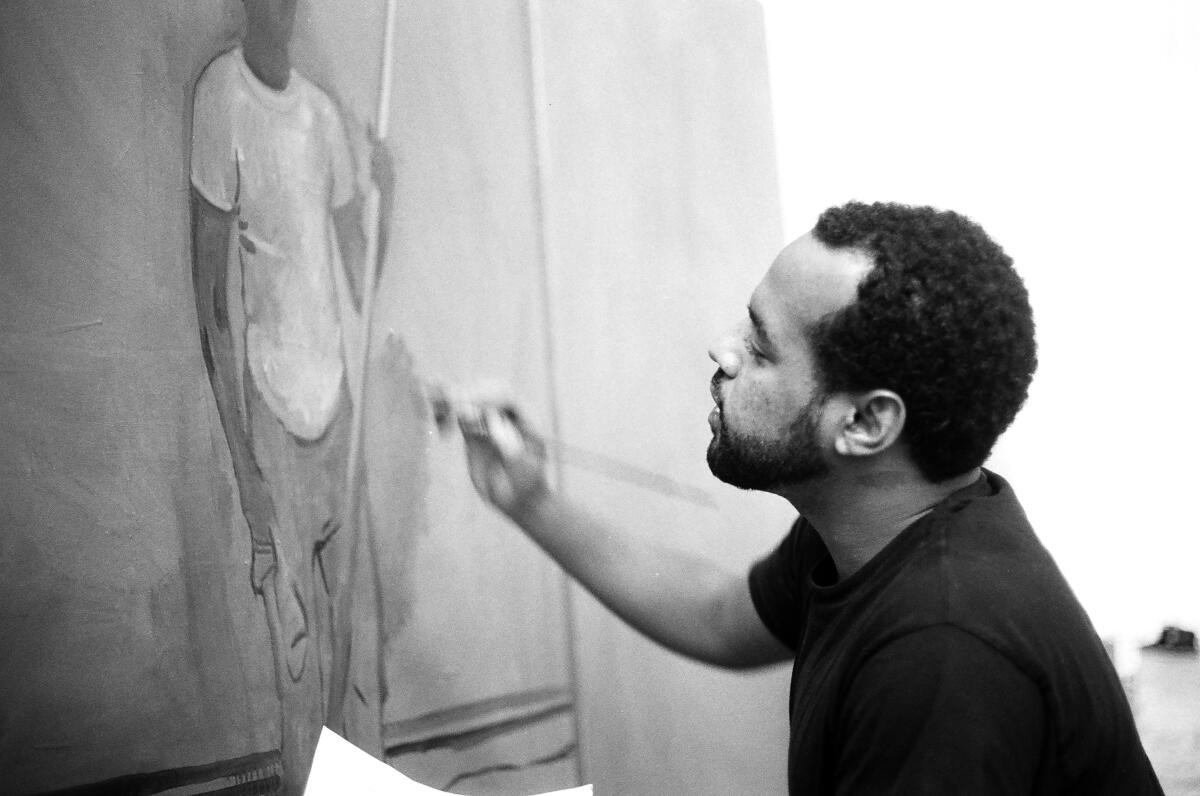 A beareded young Black man paints a figure on a canvas.