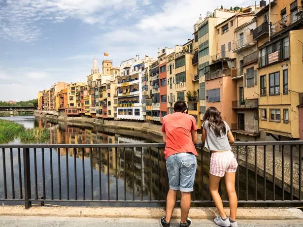 View of the Cathedral of Girona over houses besides the river Onyar painted in vivid colors, with a bridge with people crossing it.  Spain, Catalonia, Girona