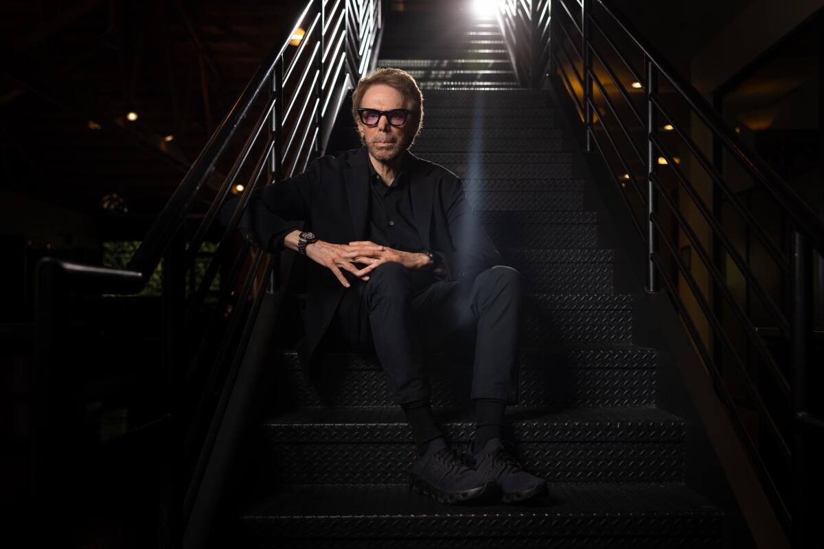 A man wearing glasses sits and poses for a portrait with his hands linked