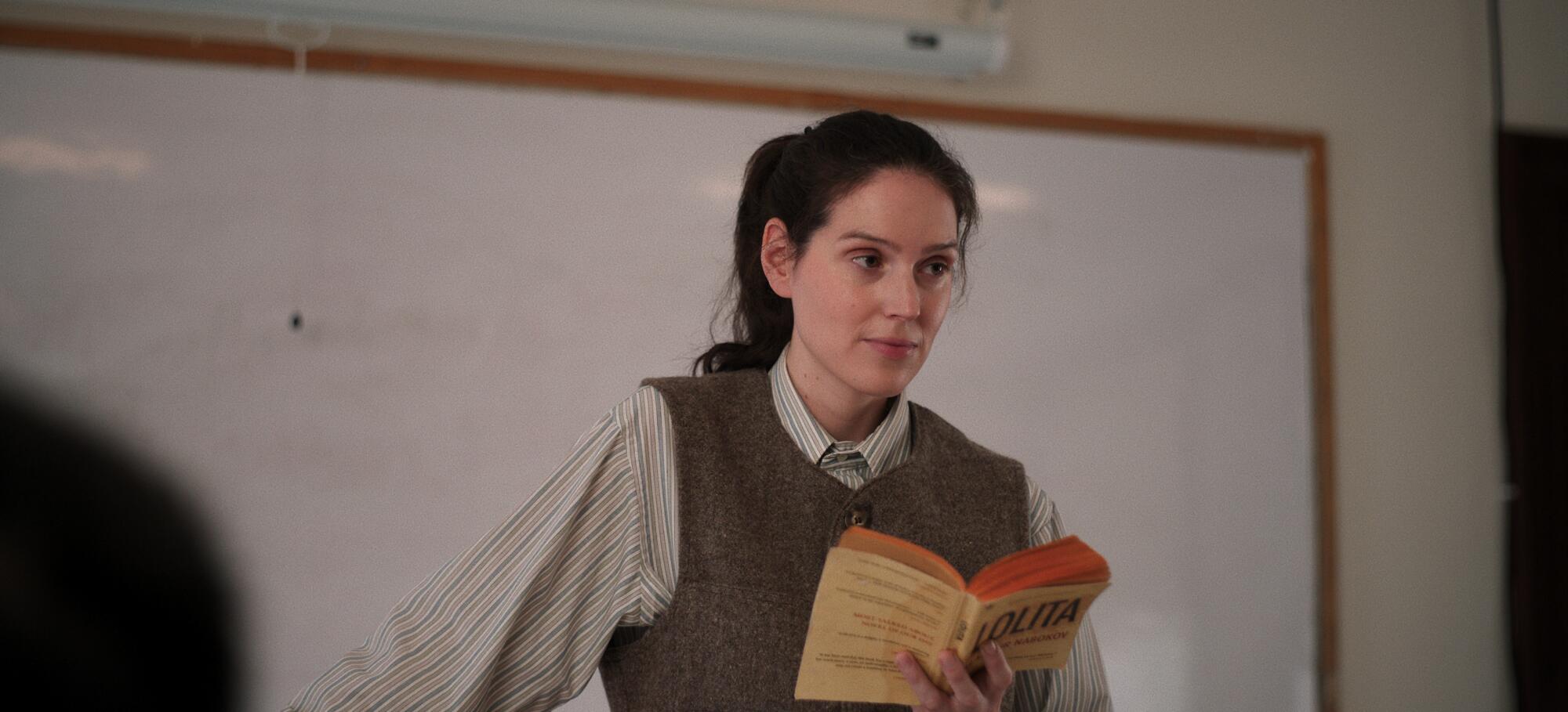 A woman reads a passage in front of a classroom.