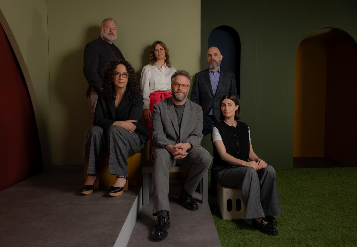 A group of men and women pose for against an olive green backdrop