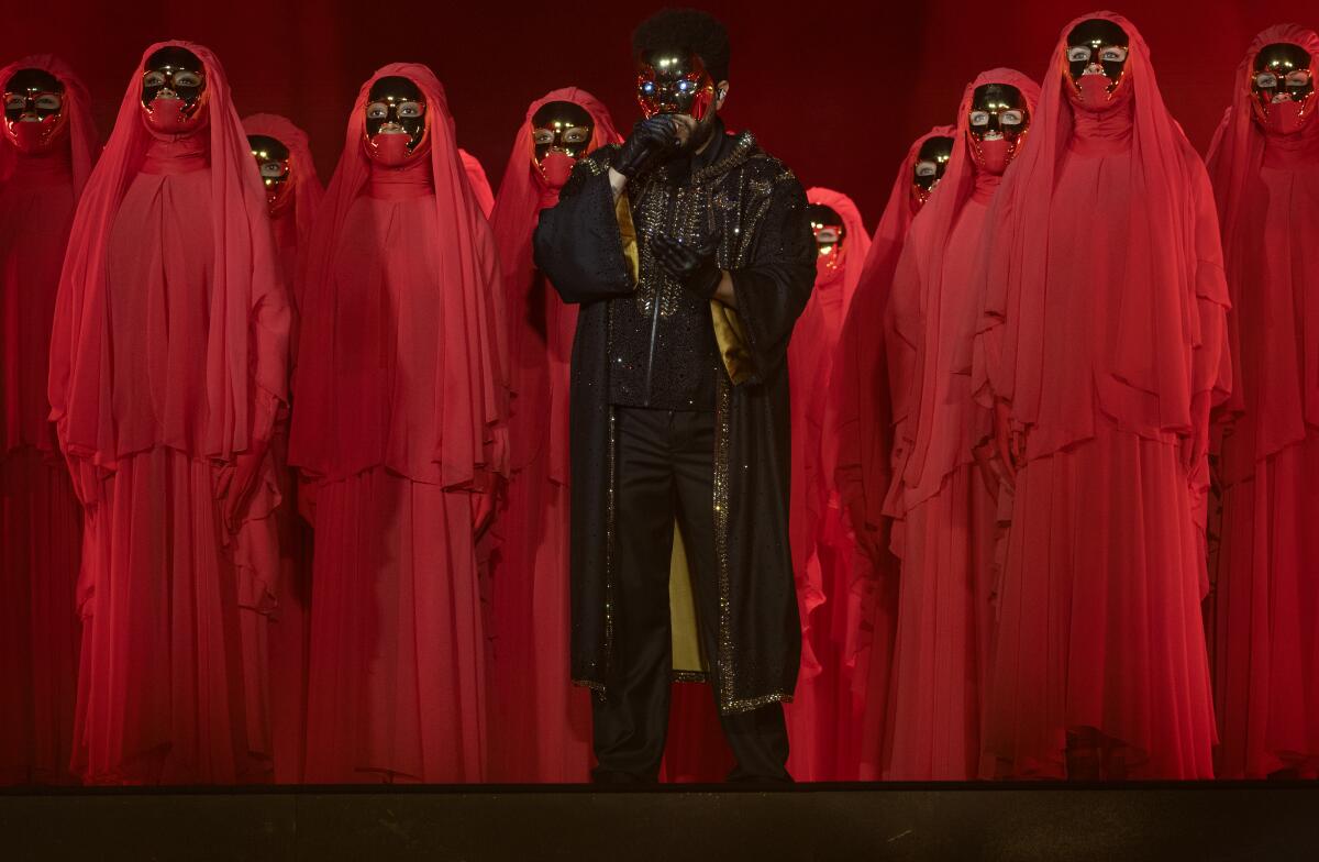 Man in a mask surrounded by people in red capes