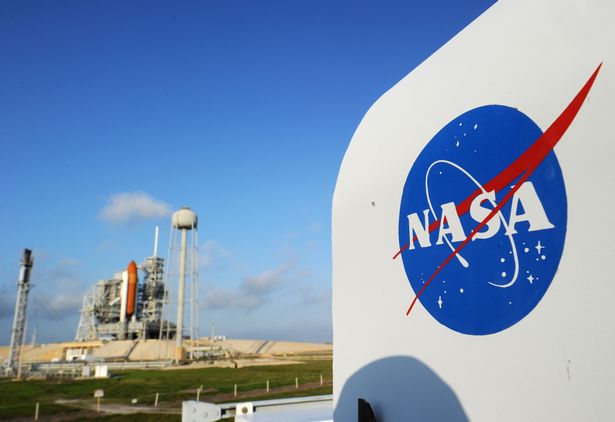 NASA's logo on a sign beside a space shuttle at Kennedy Space Center.