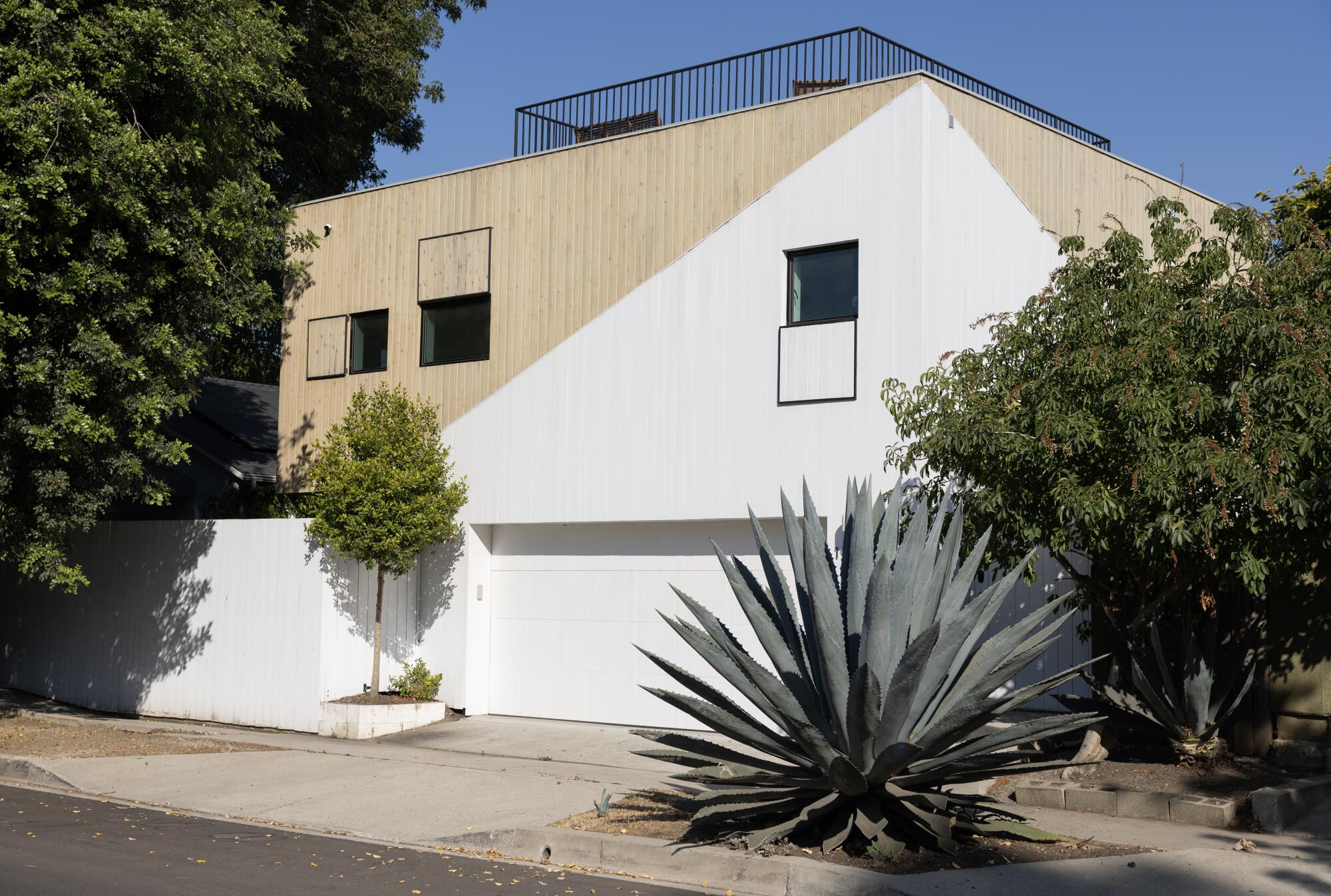 A cedar clad home with white painted fence and rooftop terrace