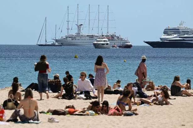 Beachogoers enjoy the sun on a beach along the Boulevard de la Croisette, as yachts and cruise ships sit anchored off the shore, on the sidelines of the 78th edition of the Cannes Film Festival in Cannes, southern France, on May 17, 2025. (Photo by Miguel MEDINA / AFP) (Photo by MIGUEL MEDINA/AFP via Getty Images)