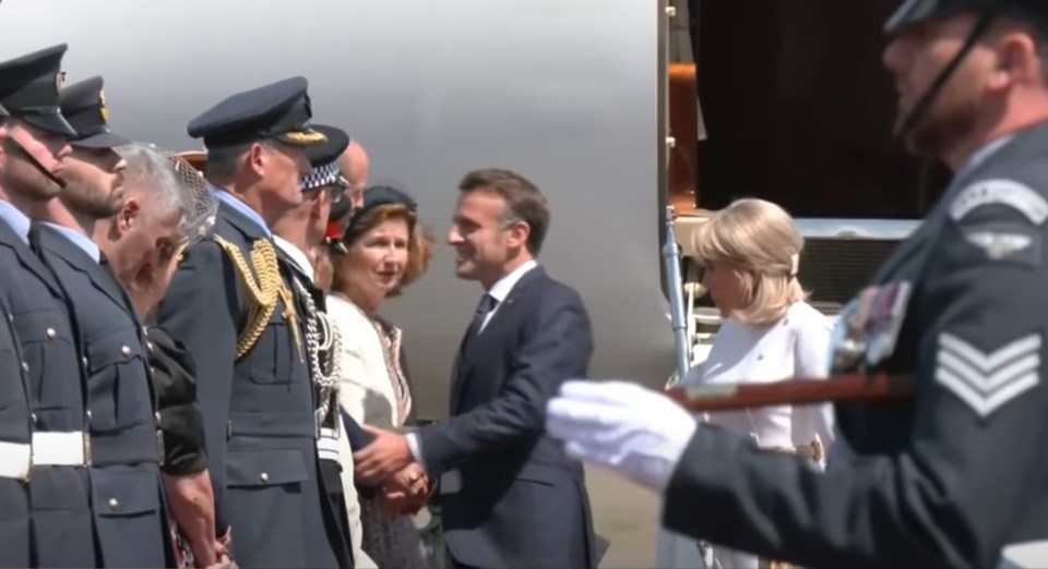 Emmanuel Macron shaking hands with someone while Brigitte Macron stands nearby.