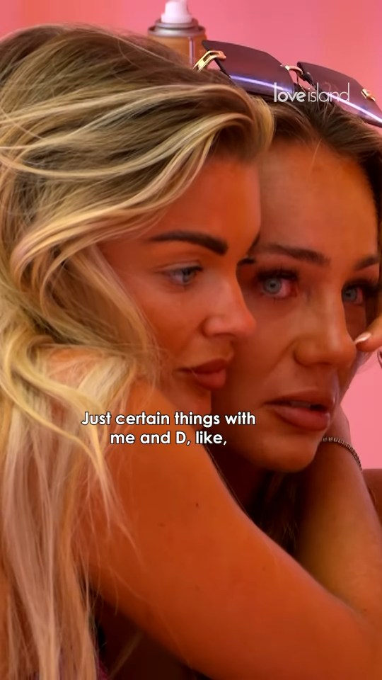 Two women embracing, one whispering.