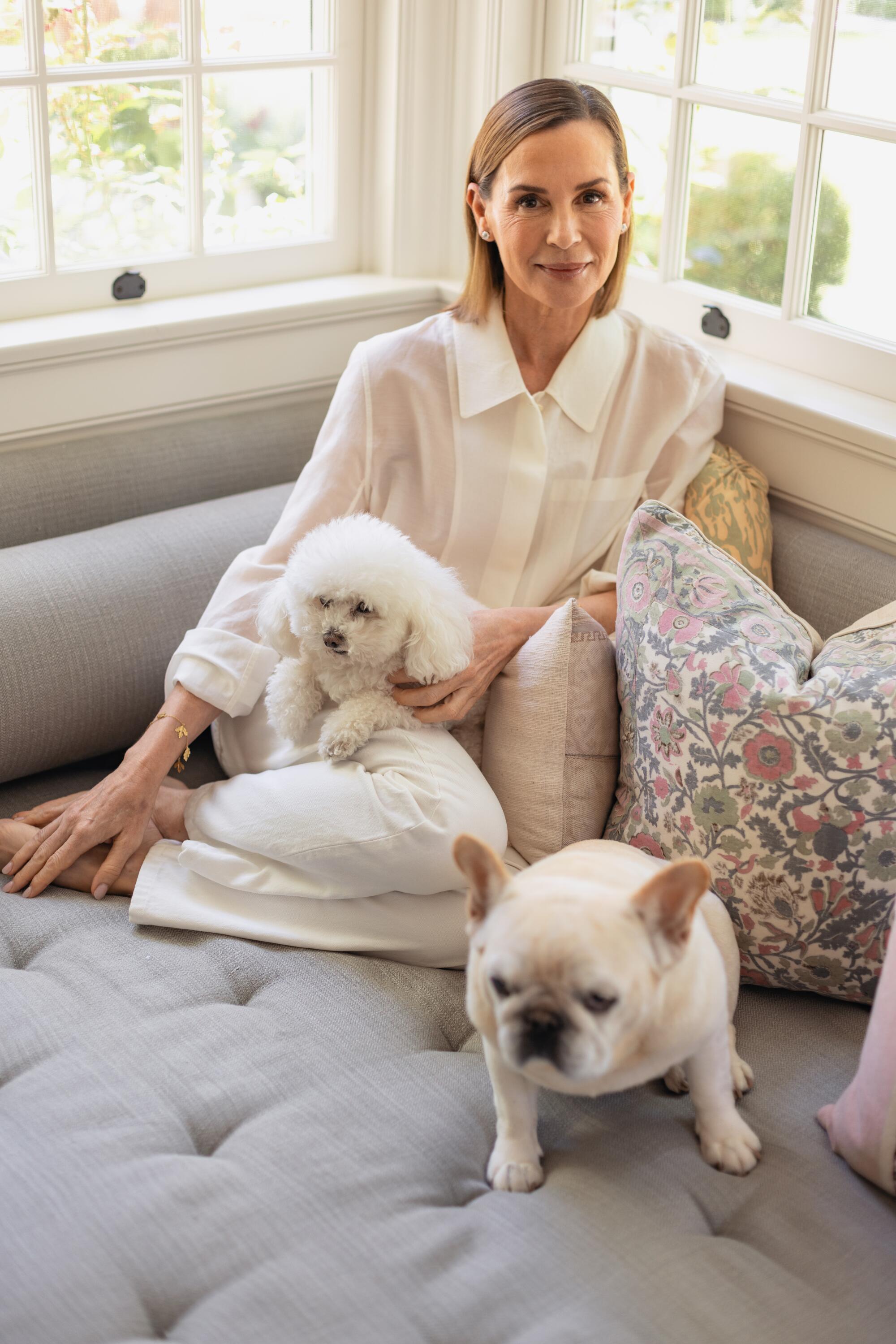 A woman sits with two sweet-looking white dogs, one a French bulldog.