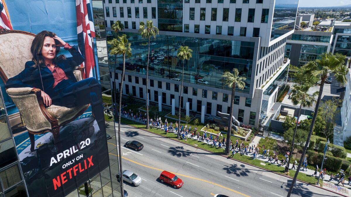 a billboard for a Netflix streaming show "The Diplomat" on a building across the street where WGA members walk a picket line