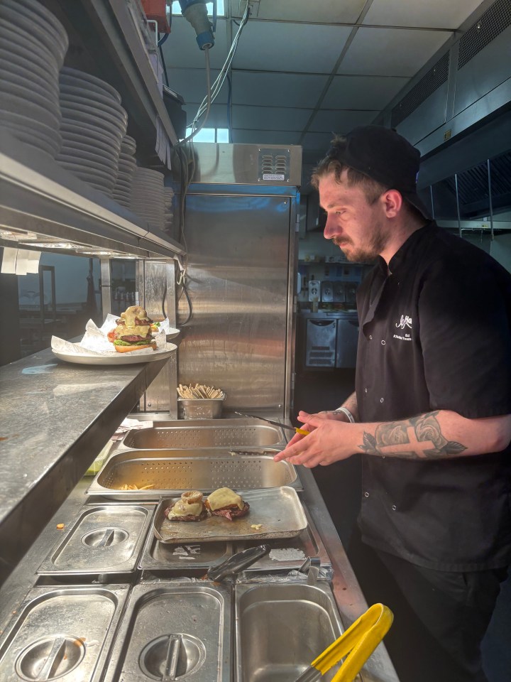 A chef prepares burgers in a restaurant kitchen.