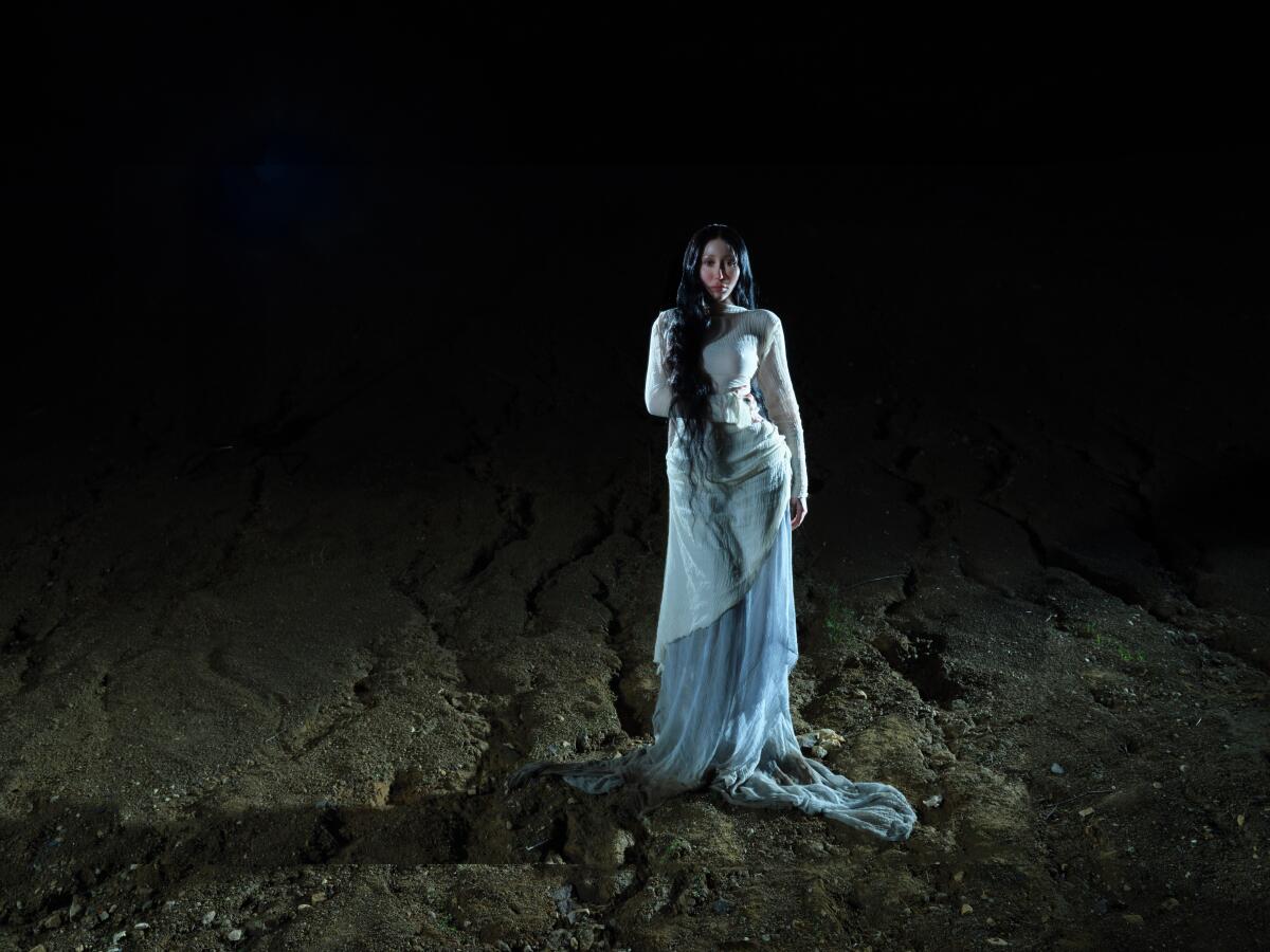 Woman in a white dress standing in dirt.