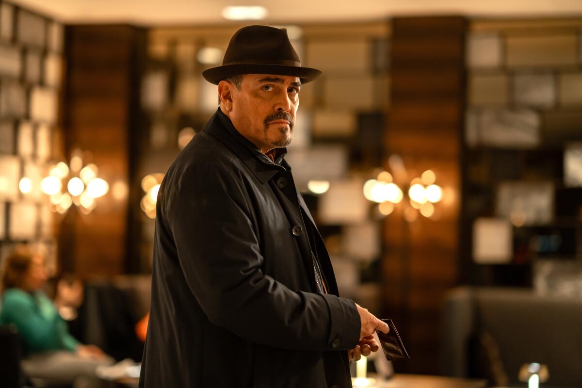 A goateed man wearing a black jacket and a black hat 