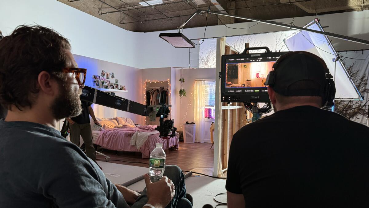 Two men look at a camera screen on the set of recreated house.
